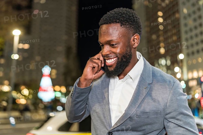Young businessman smiling and chatting on a mobile phone while enjoying the vibrant city nightlife, surrounded by twinkling lights