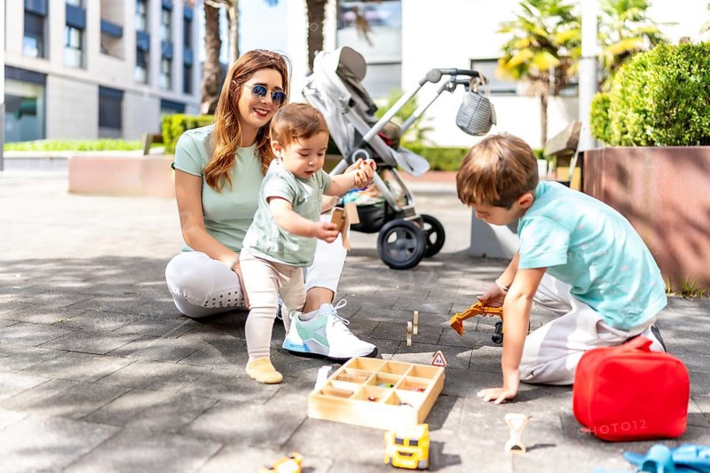 Full length photo of a happy woman and sons playing with toys in an urban space