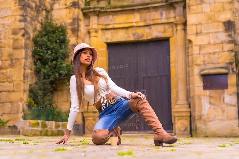 A young Latin woman with a white t-shirt, jeans and a hat enjoying the summer holidays, with a take away cafe, posado de moda, Pasaje San Juan, Gipuzkoa, Pais Vasco