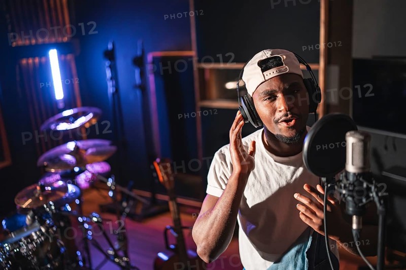 Young man recording vocals using a professional microphone and headphones in a music studio