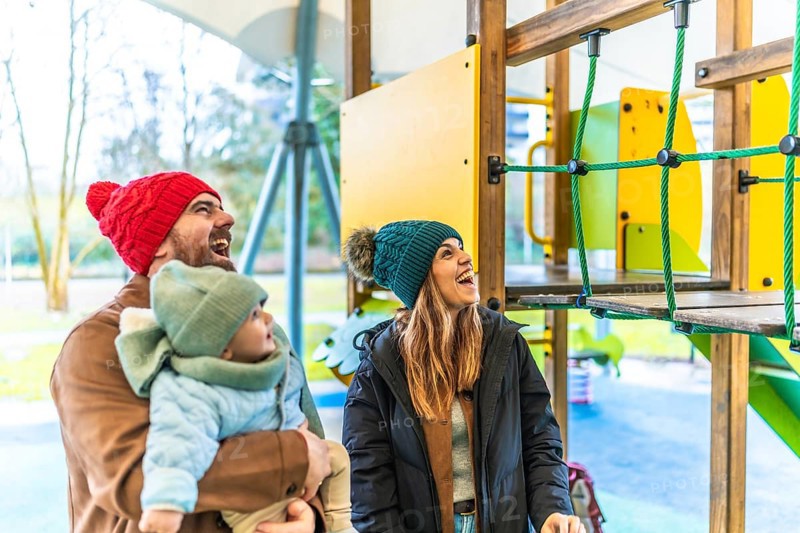Cheerful parents and their baby are enjoying a playful day at the playground during wintertime