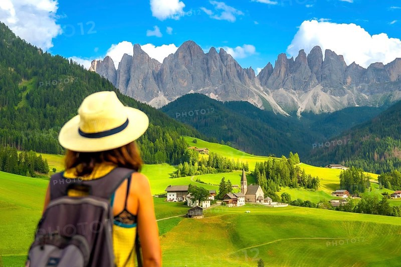 Woman with a backpack enjoying the serene summer landscape of santa maddalena village in val di funes, dolomites, italy