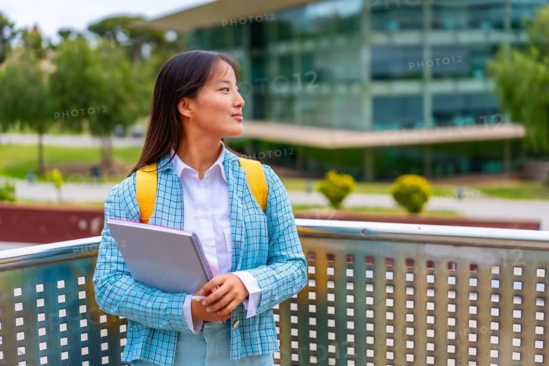 Three quarter length portrait of a beauty female chinese student looking away distracted standing in the university campus