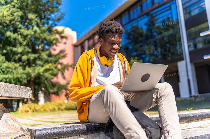 African man sitting at staircases on the university campus studying using laptop