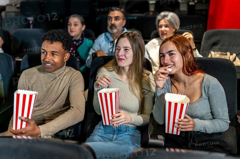 Group of friends watching a film at the movie theatre, eating popcorn and enjoying their leisure time
