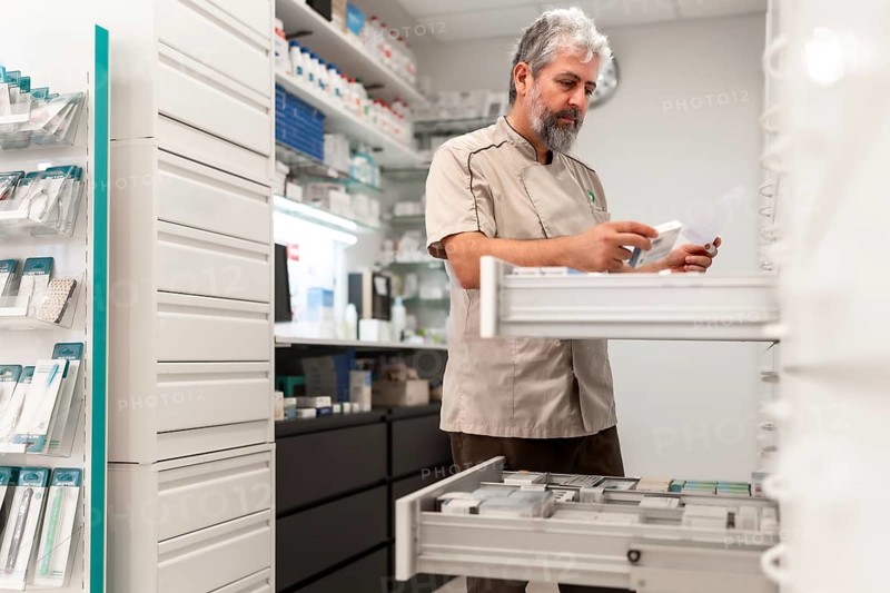 Male mature pharmacist working in storage room searching for medicines in a drawer