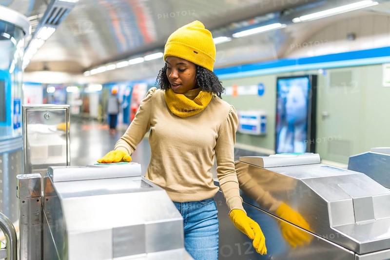 Young black woman wearing yellow woolen hat and gloves validating electronic ticket to enter subway station