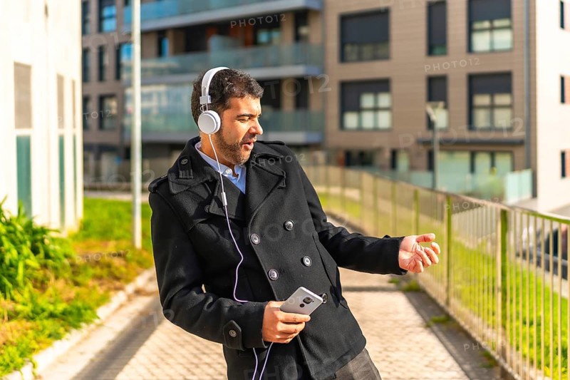 Adult caucasian businessman in casual winter clothes dancing while listening to music with mobile phone and headphones in the city
