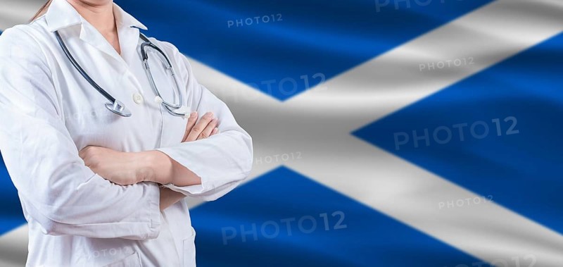 Doctor with crossed arms on Scottish flag. Scotland health and care concept. Female doctor on Scottish flag