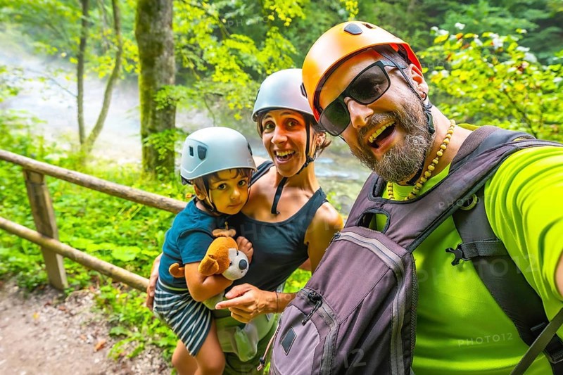 Happy family wearing helmets taking a selfie while hiking on a trail next to a river in vintgar gorge, bled, slovenia