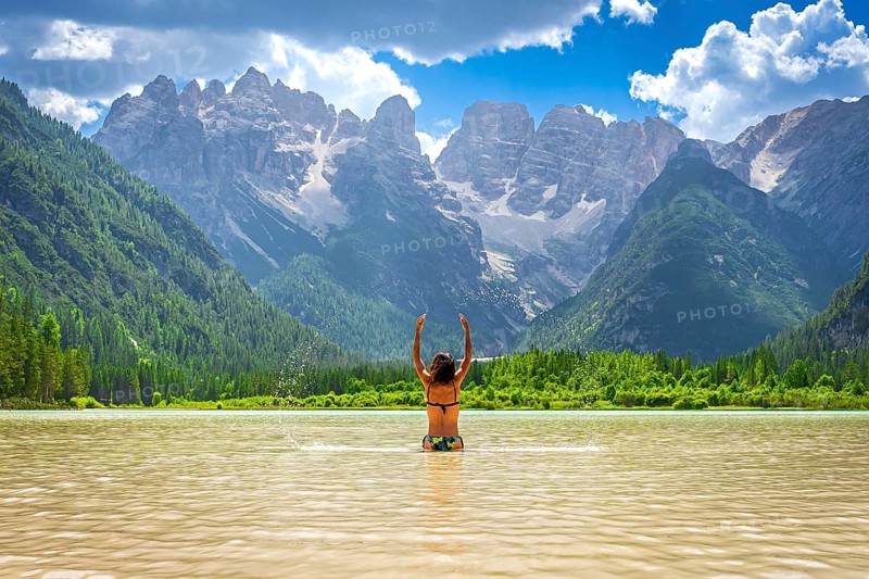 Tourist raising arms in the durrensee lake, enjoying summer holidays in the dolomites, italy