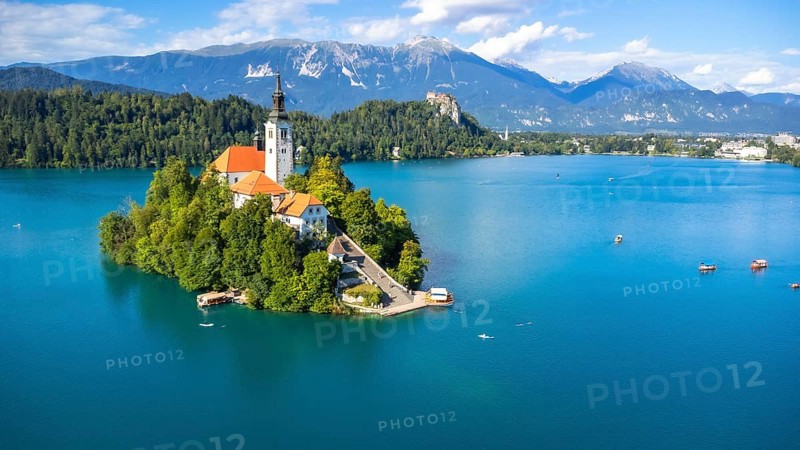 Aerial view of lake bled island with pilgrimage church of the assumption of maria on a sunny summer day with julian alps and bled castle in the background