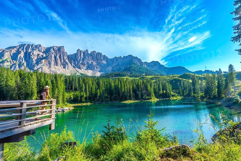 Female tourist admiring the stunning turquoise waters of lake carezza with the latemar mountain range in the background, dolomites, italy