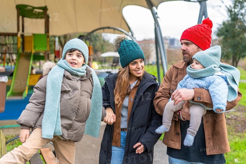 Happy family enjoying a delightful winter day at the playground, bundled up in warm clothes, sharing smiles and laughter together