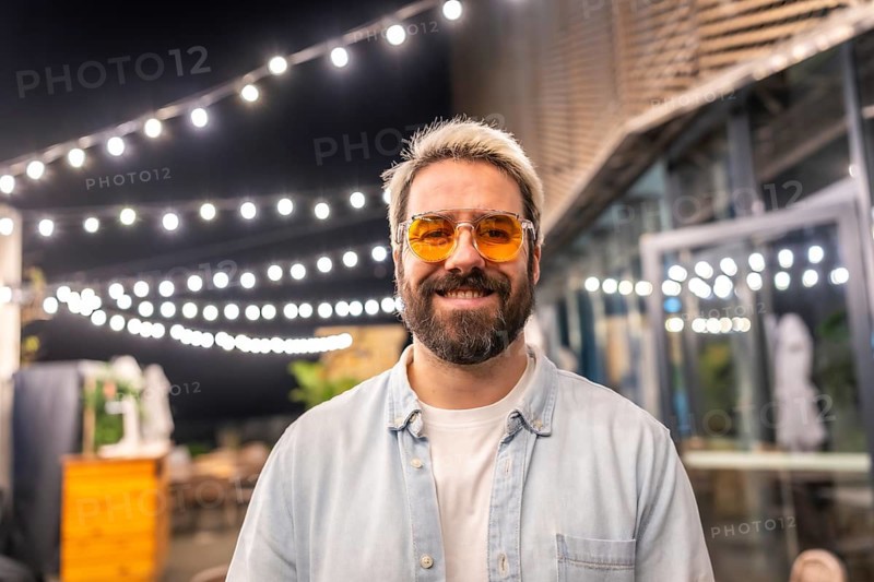 Hipster caucasian man with modern sunglasses smiling in a bar terrace at night