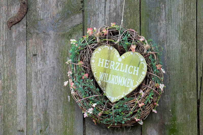 A heart-shaped welcome sign in a wreath with flowers, attached to a wooden surface, North Rhine-Westphalia, Germany, Europe