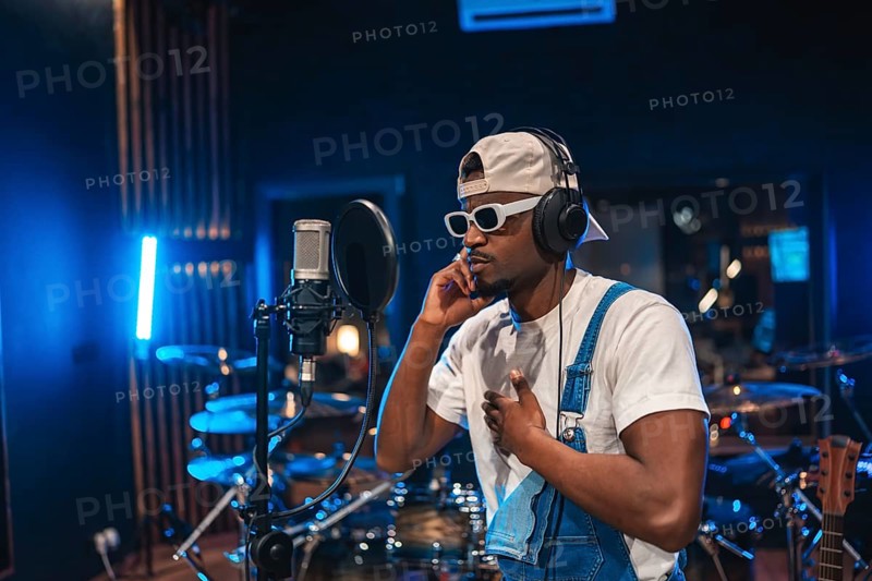 Young, stylish male artist passionately recording a song in a professional music studio, surrounded by modern equipment and vibrant lights