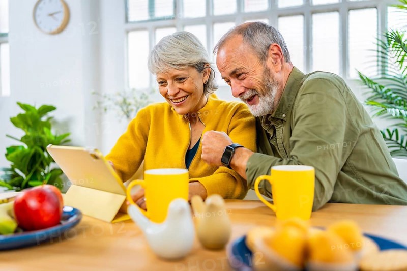 Happy married senior couple using tablet together while sharing breakfast at home