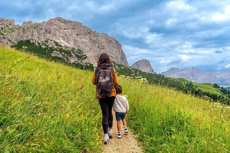 Mother and son walking on a path surrounded by lush green grass, enjoying the breathtaking view of the dolomites mountains in gardena pass
