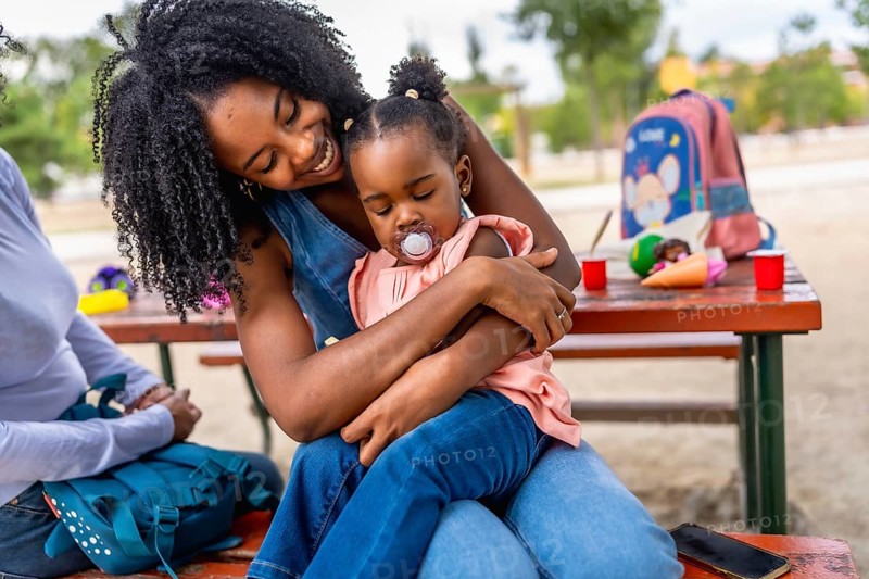 Happy african woman embracing her baby daughter in the park sitting on a picnic table