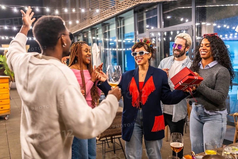 Multiracial friends celebrating surprise birthday party for a woman at night in the terrace of a bar