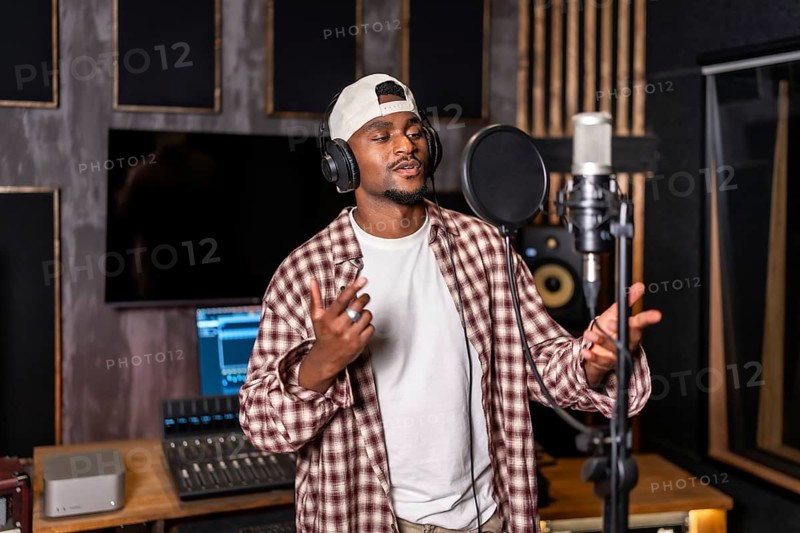 Young artist wearing headphones and singing into microphone while recording a song in professional music studio