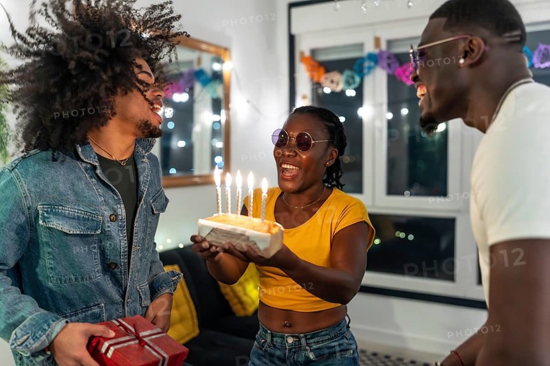 Young multiracial people surprising a friend with birthday cake and gift during night party at home