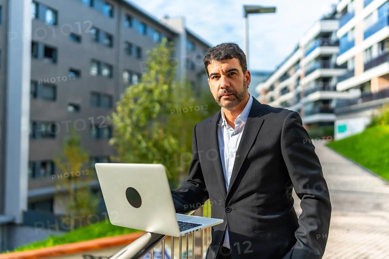 Portrait of a mature adult caucasian elegant and confident businessman using laptop standing in the city