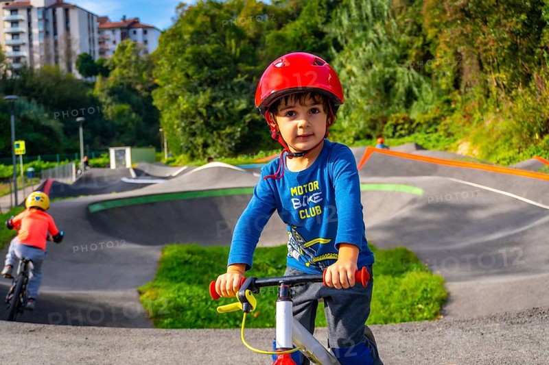 A young boy in a blue shirt and helmet is riding a bike on a dirt track. The boy is smiling and he is enjoying himself