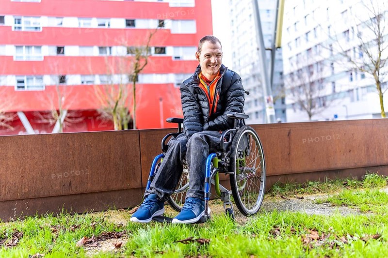 Young man with disability smiling in his wheelchair enjoying a day out in an urban park, promoting inclusivity and accessibility