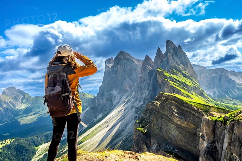 Hiker shielding her eyes while enjoying the breathtaking view of the odle mountain range in the dolomites, italy, during a sunny summer day