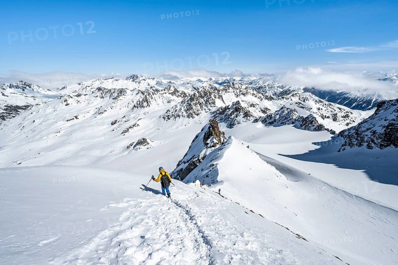 Mountaineer with ice axe and crampons, descent through steep snowfield on Piz Kesch or Piz d'Es-cha in winter, view of mountain panorama with Vadret da Porchabella glacier, Albula Alps, Rhaetian Alps, Grisons, Eastern Switzerland, Switzerland, Europe