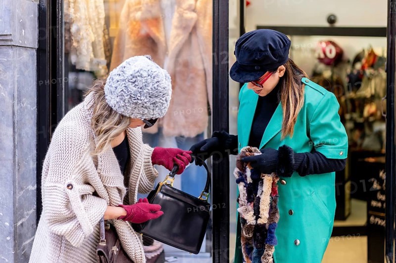 Young blonde girl shopping in the city and served by a shop assistant, looking at shop windows of clothing stores. Sunglasses and red gloves