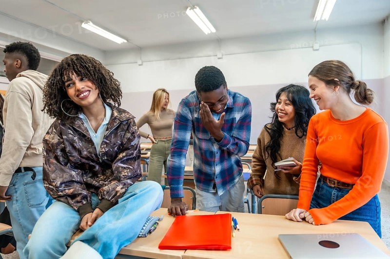 Cheerful multi ethnic university students enjoying time together, laughing and studying in a classroom