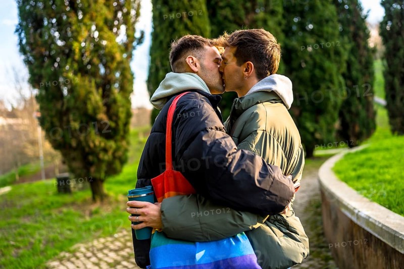 Two men are kissing in a park, embracing each other tenderly, showcasing their love and commitment