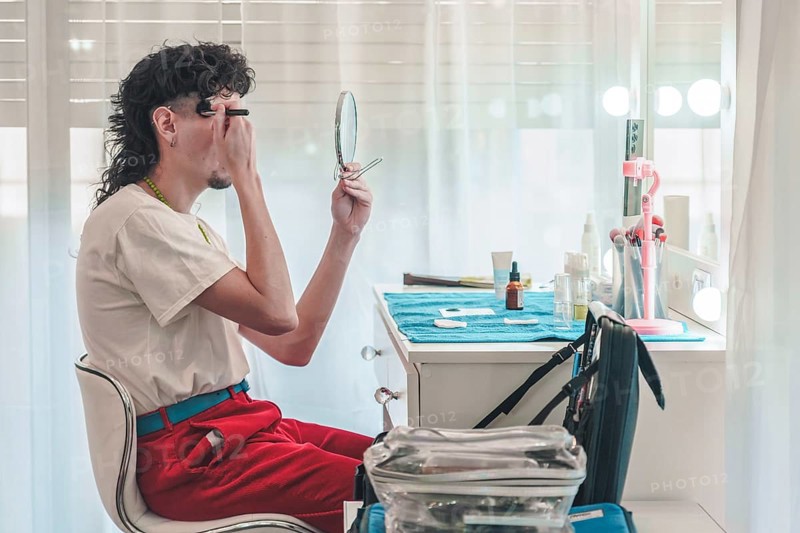 Young make-up artist applying eyebrow pencil while looking in a mirror and getting ready for a performance, showcasing diversity and inclusion in the beauty industry