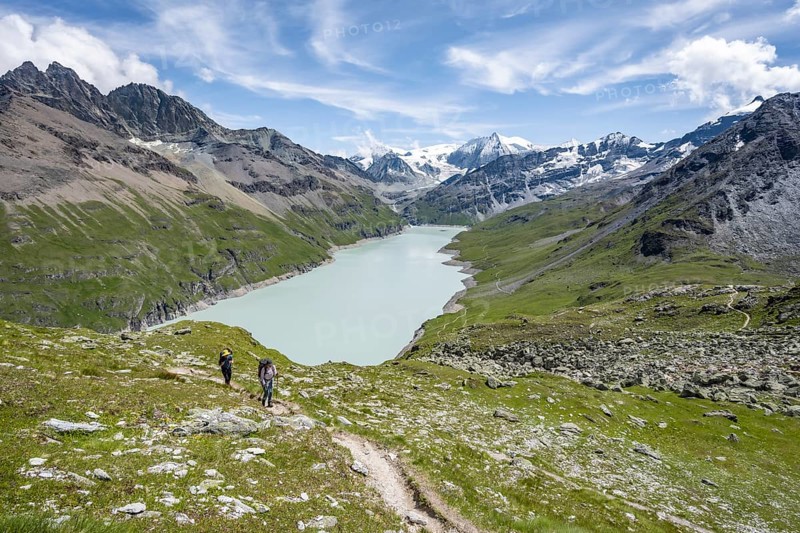 Two mountaineers on a hiking trail, view of a blue mountain lake, Lac des Dix reservoir, mountain peak Mont Blanc de Cheilon in the background, Hérménence, Valais Alps, Valais, Switzerland, Europe