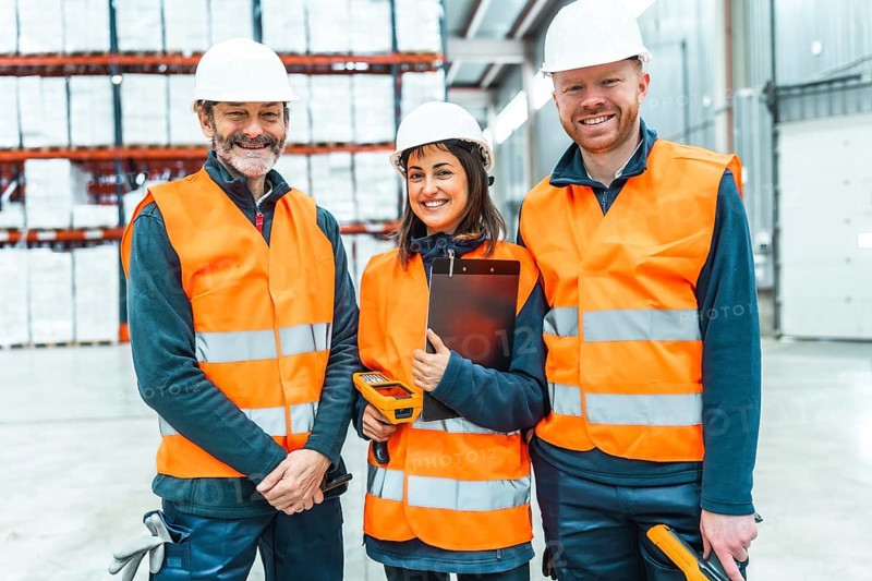 Warehouse workers wearing safety vests and hard hats smiling in a logistics center, managing inventory and shipments