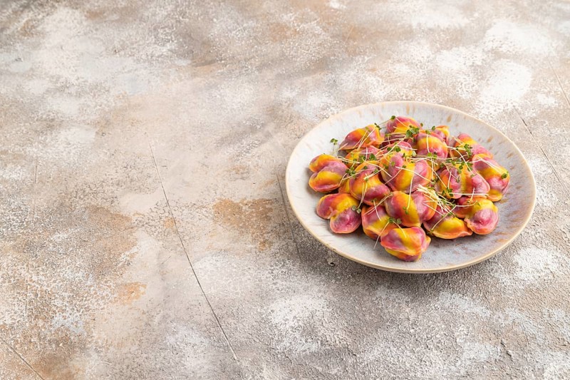 Rainbow colored dumplings with pepper, herbs, microgreen on brown concrete background. Side view, copy space