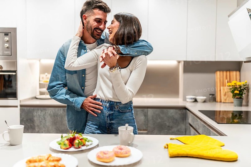Young couple hugging and laughing in their modern kitchen, enjoying a romantic moment together with breakfast ready on the counter