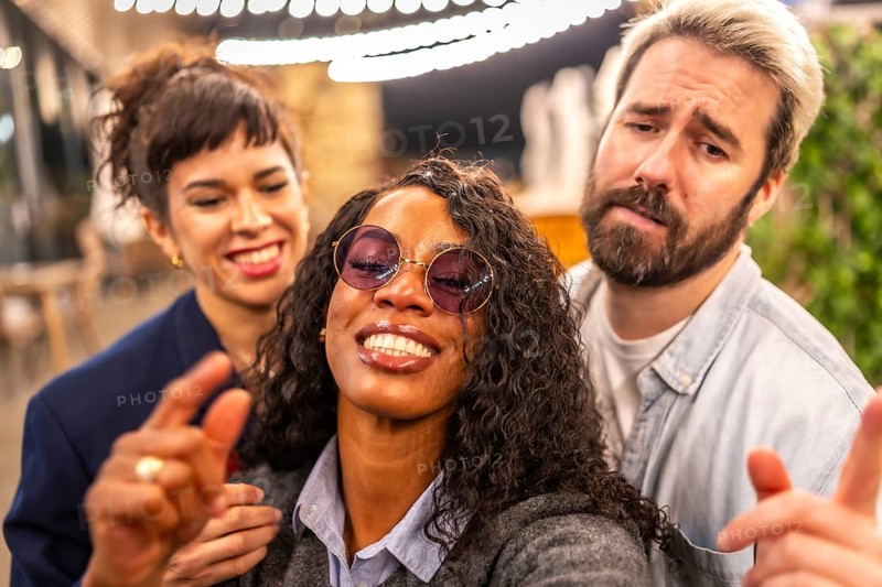 Close-up and personal point of view of multi-ethnic friends pulling funny faces while taking selfie in night party outdoors