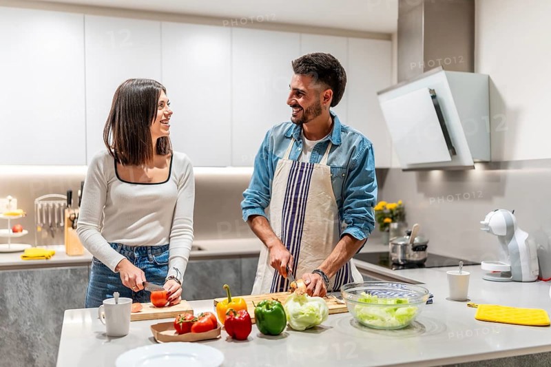 Young smiling couple preparing a healthy salad together in their modern kitchen, enjoying their time and sharing a moment of complicity