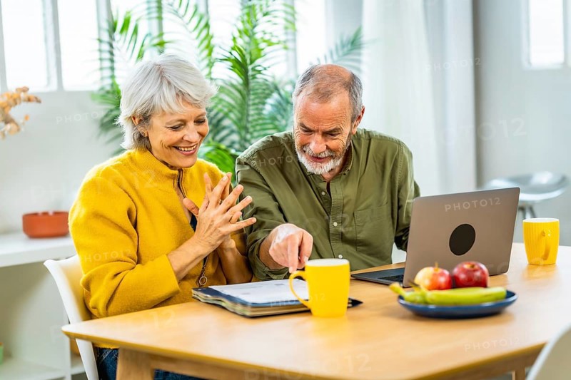 Senior couple going over their finances while sitting on their living room expressing happiness analyzing the data