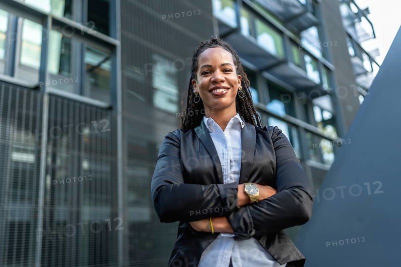 Migrant latin confident woman standing with arms crossed smiling at camera in a financial district