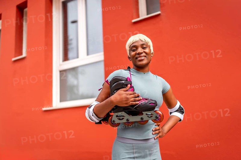 Portrait of african female skater with inline skates on shoulder standing outdoors next to red building