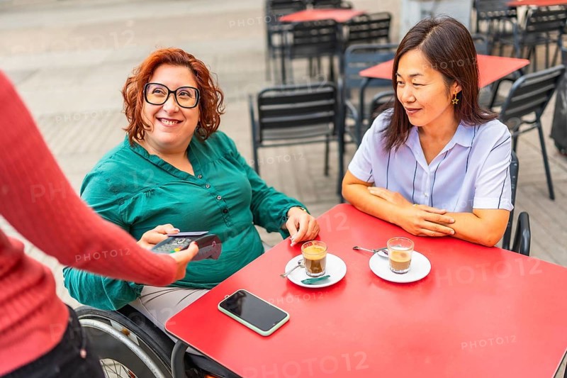 Woman with disability and asian friend paying with credit card in a sidewalk cafeteria
