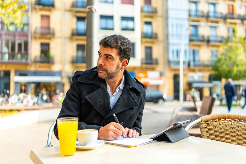 Mature handsome caucasian businessman writing notes and using digital tablet sitting on an outdoors cafeteria