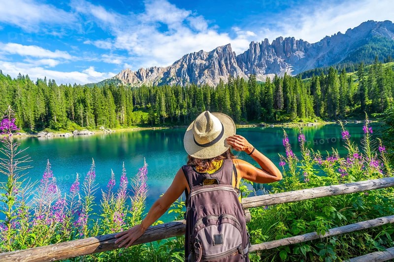 Female tourist admiring the stunning turquoise waters of lake carezza with latemar mountain range in the background, dolomites, italy