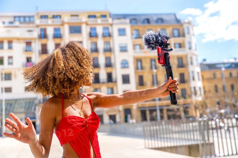 Female latin young vlogger recording a video in the city using mobile phone and microphone