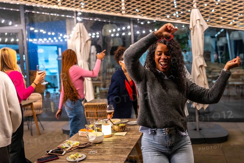 Latin woman dancing happily while partying with diverse friends in a roof bar at night